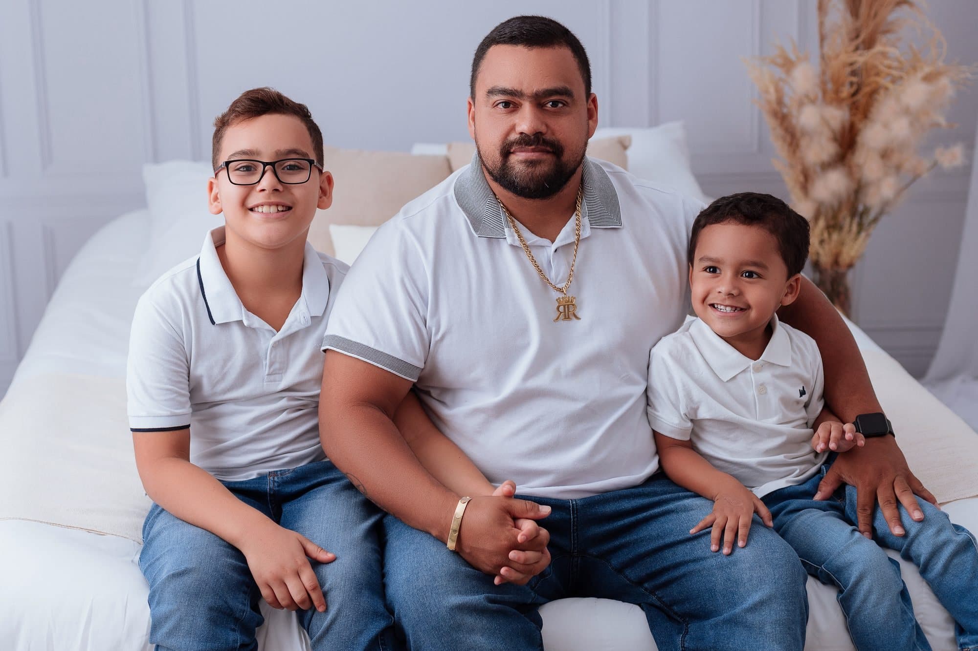 Gabriel deitado ao lado do pai e do irmão, todos sorrindo
